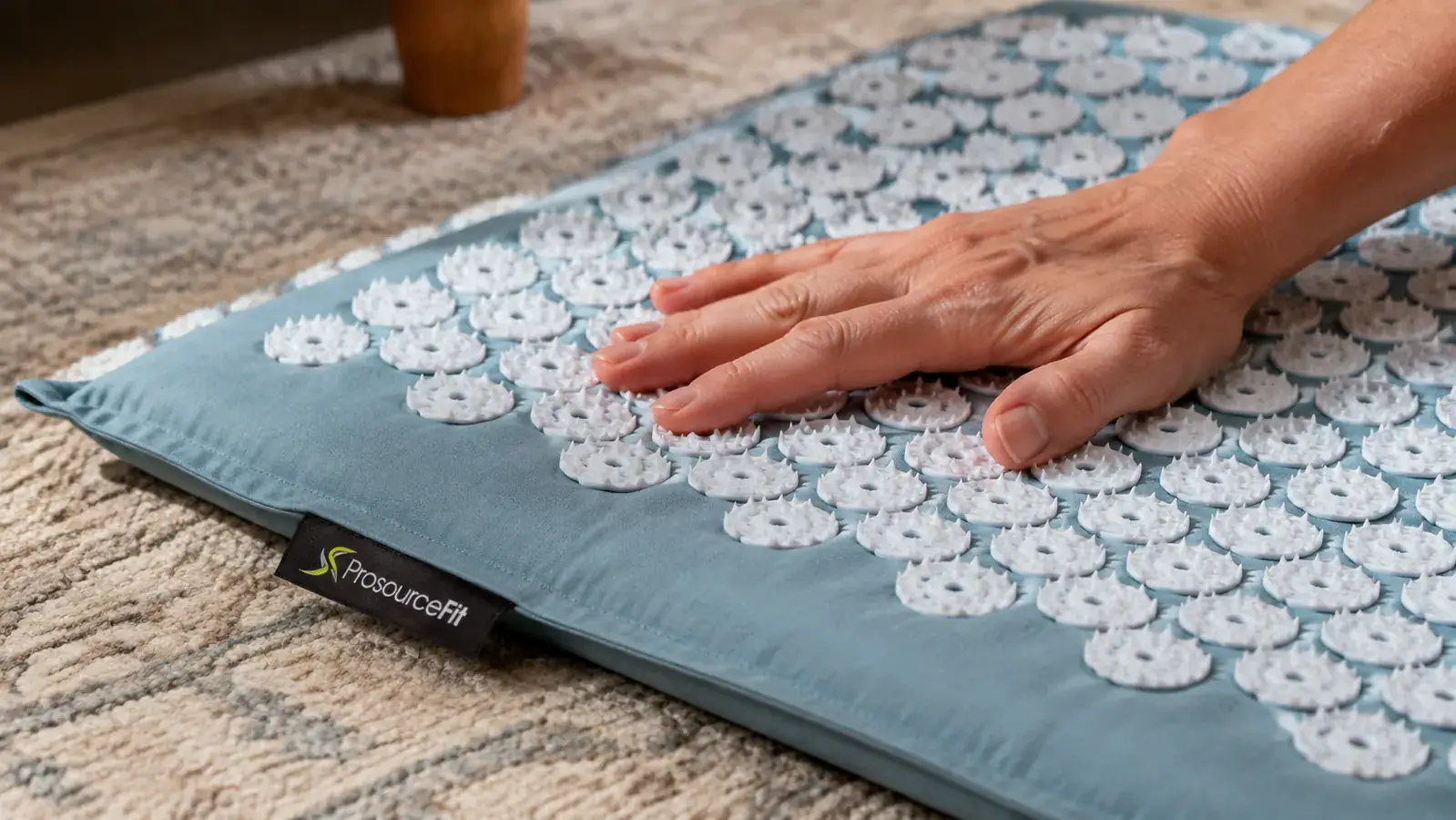 Close-up of a hand pressing down on the plastic spike tiles of an acupressure mat on a living room rug