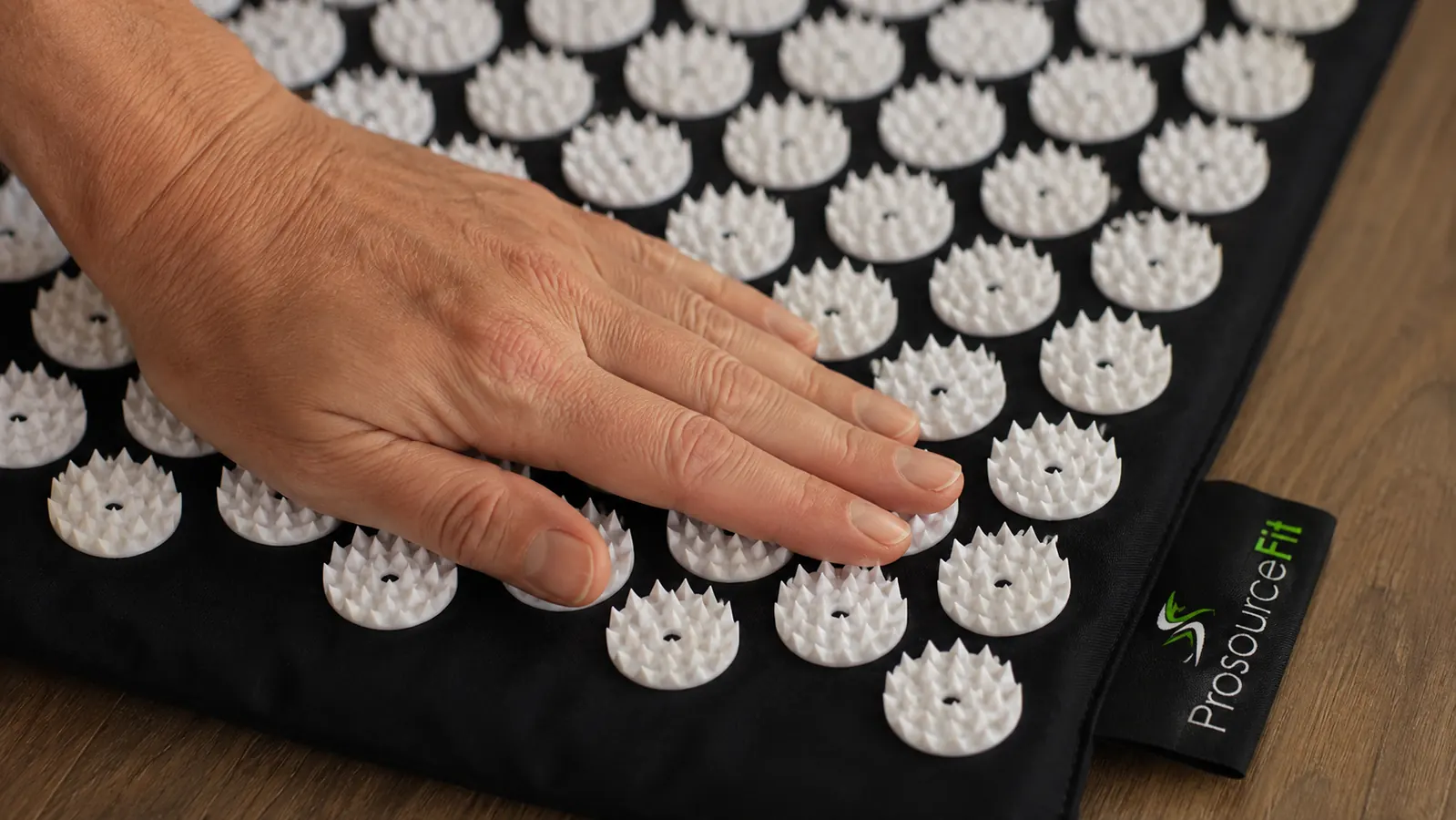 Close-up of a hand pressing down on the plastic spikes of an acupressure mat on a wood floor