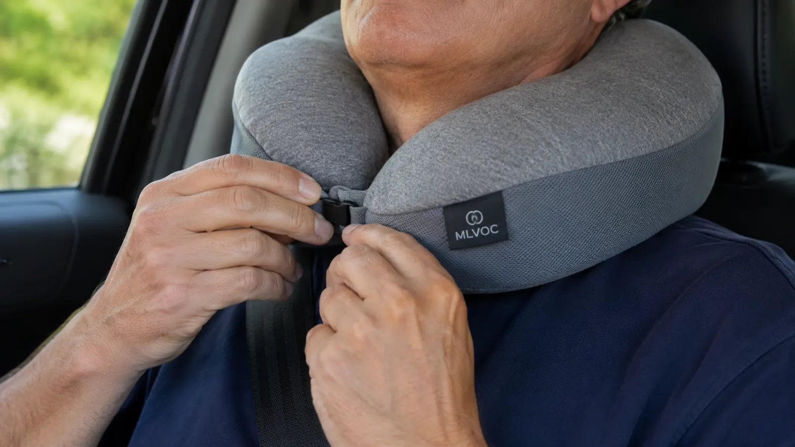 Close view of hands adjusting an MLVOC gray travel neck pillow around the neck while seated in a car
