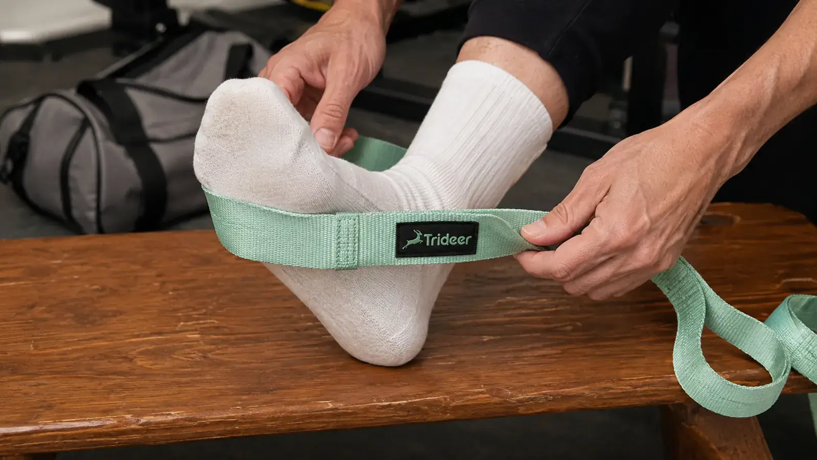 Close-up of hands adjusting a stretch strap loop around a sock-covered foot on a gym locker room bench