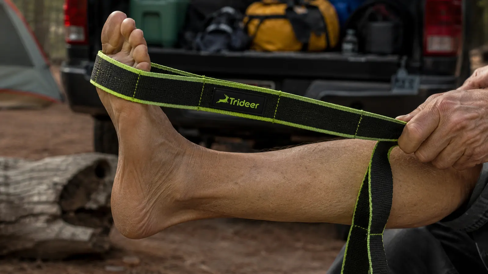 Hand looping a Trideer stretch strap around the ball of a foot while lying on a truck tailgate