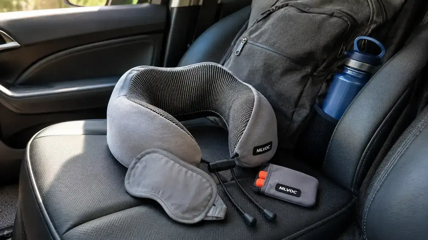 Close-up of the MLVOC travel neck pillow, eye mask, and earplugs laid out on a car passenger seat before a road trip